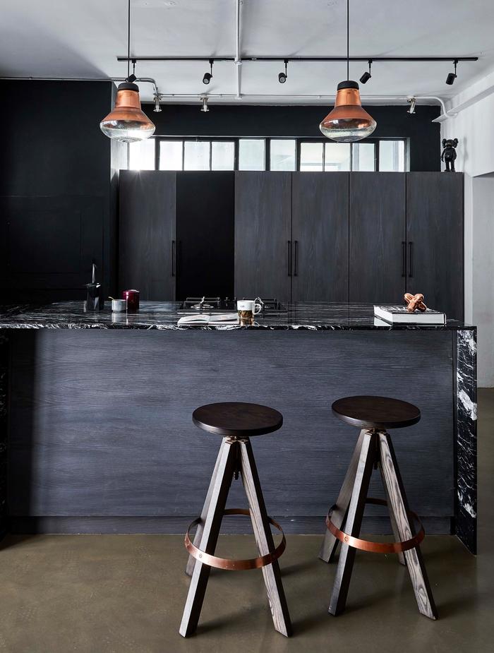 A black kitchen with white ceilings and brass hanging lamps