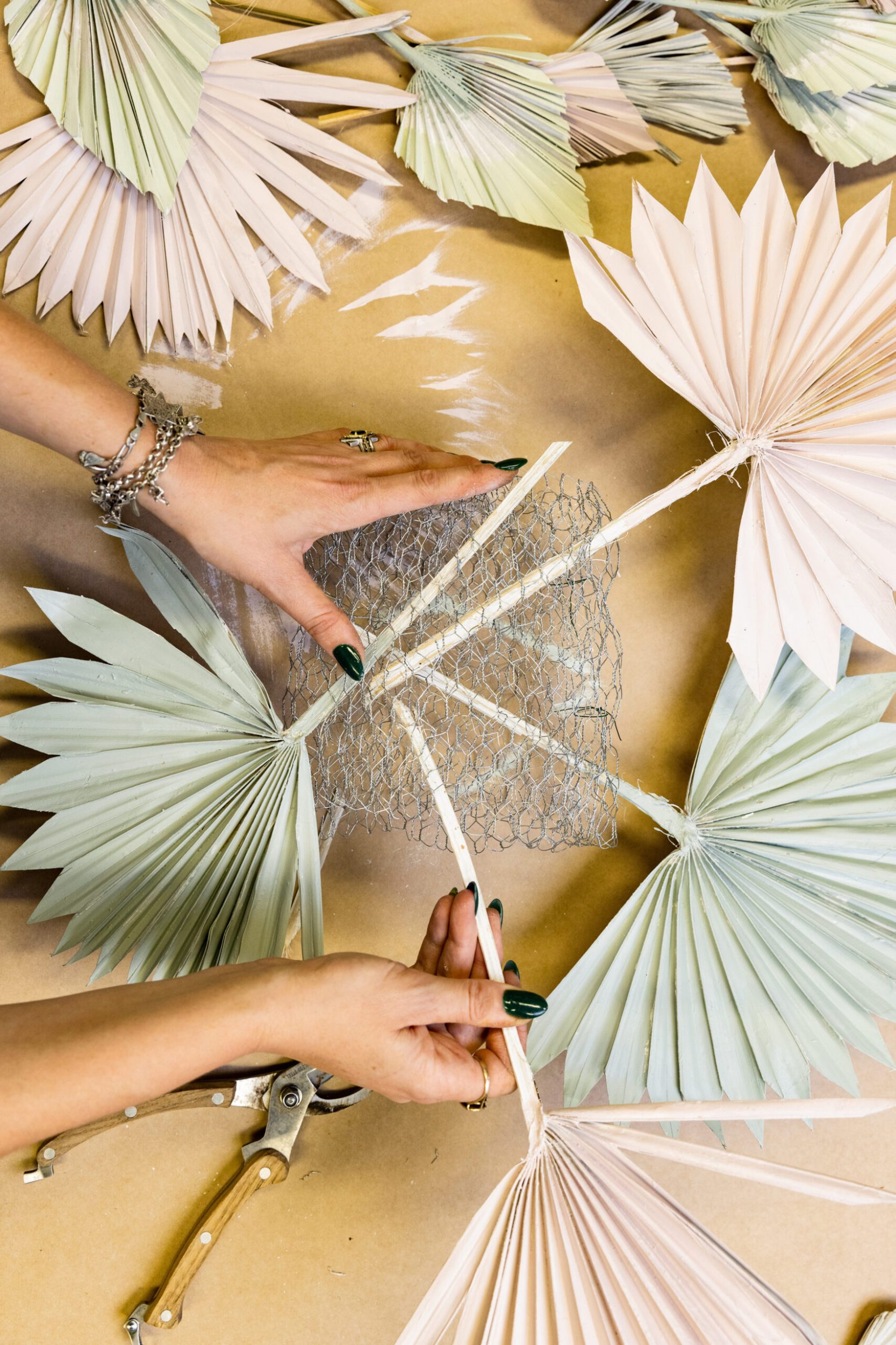 Pastel coloured painted plant fronds being threaded through chicken wire