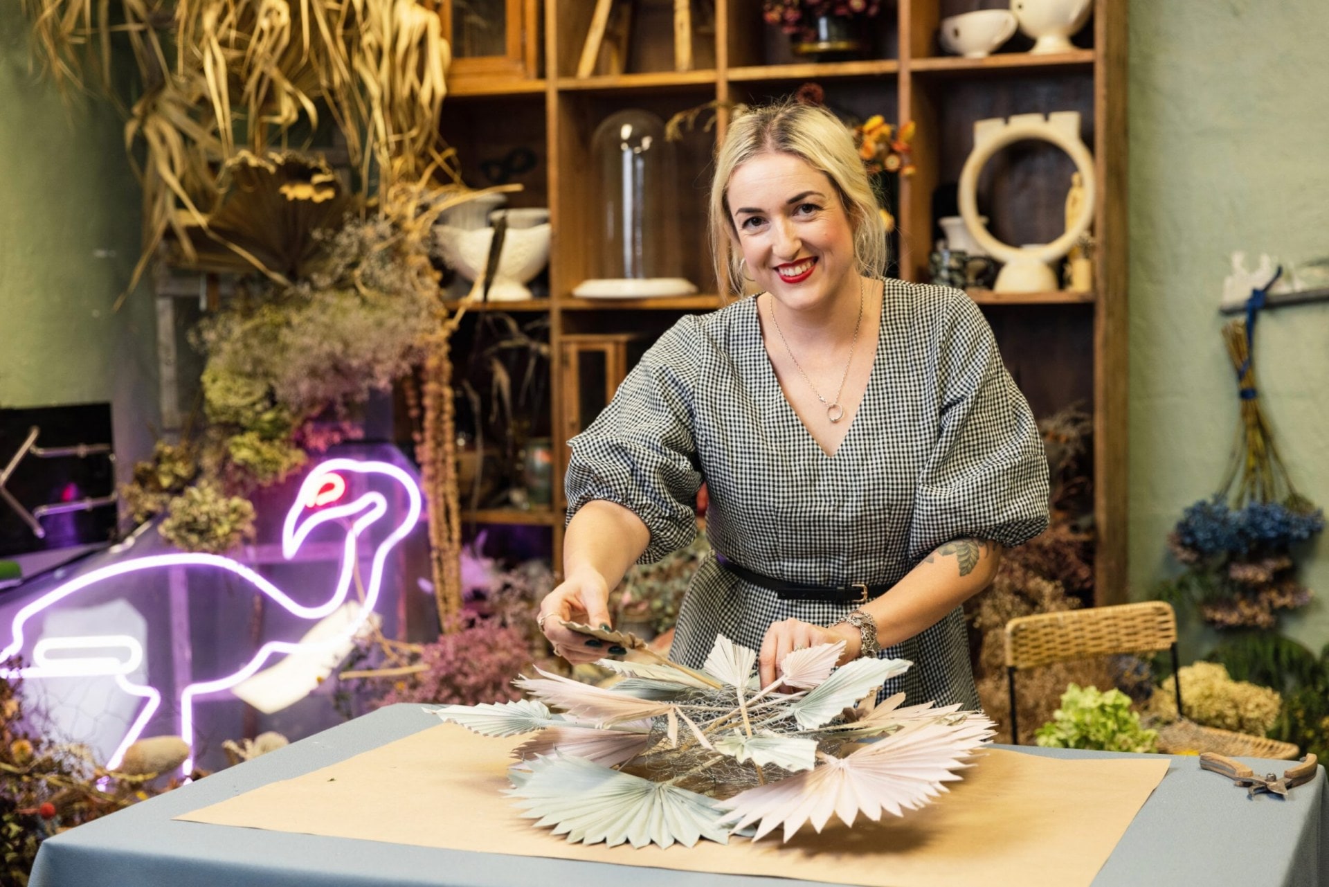 Georgie Maylon threading through plant fronds through chicken wire while smiling at camera 