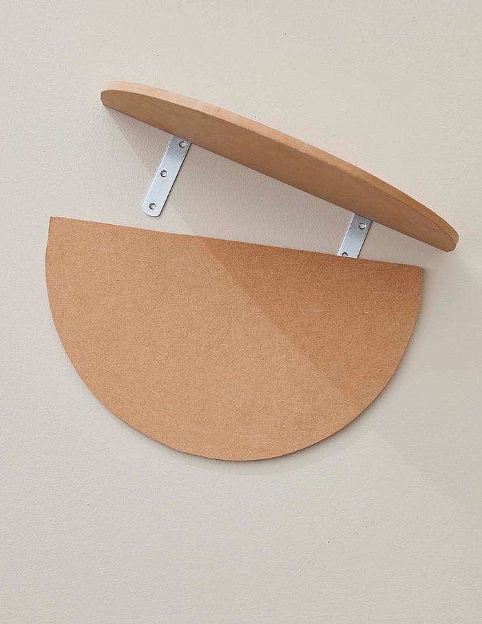 An oval MDF board hanging on wall with another piece being attached 