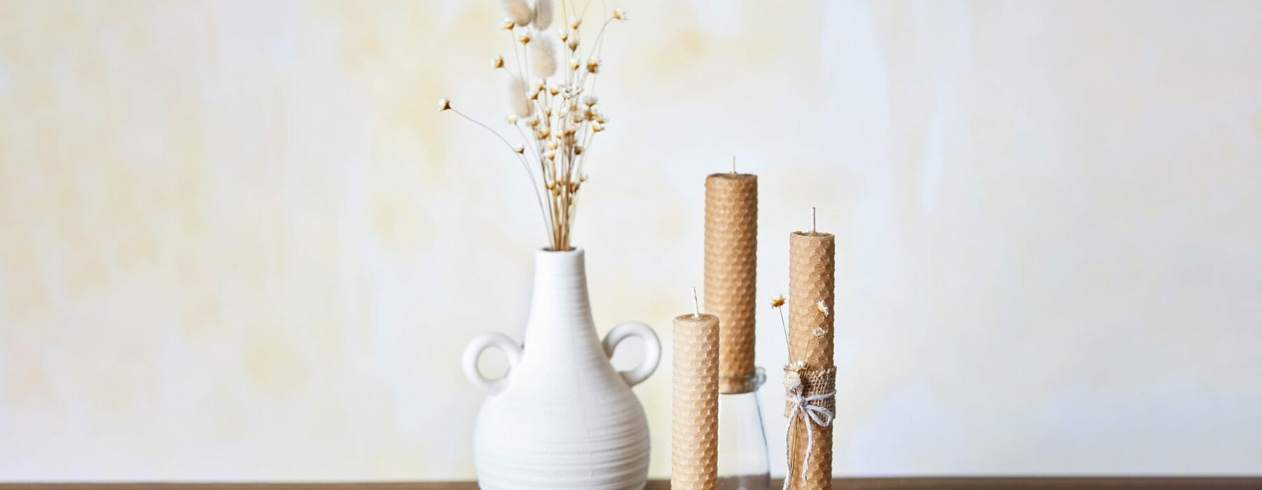 A white vase surrounded by honey candles