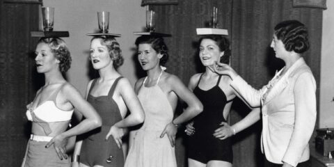 women standing with books balanced on their heads